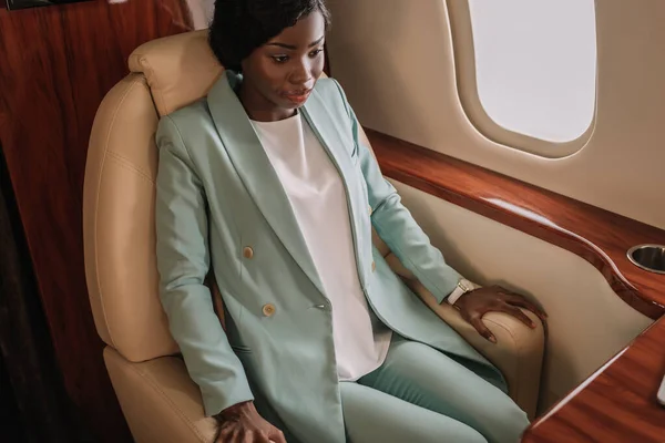 Asustada, preocupada mujer de negocios afroamericana sentada en avión privado - foto de stock