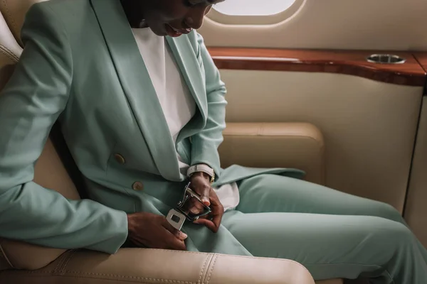 Vue recadrée d'une femme d'affaires afro-américaine attachant sa ceinture de sécurité dans un jet privé — Photo de stock