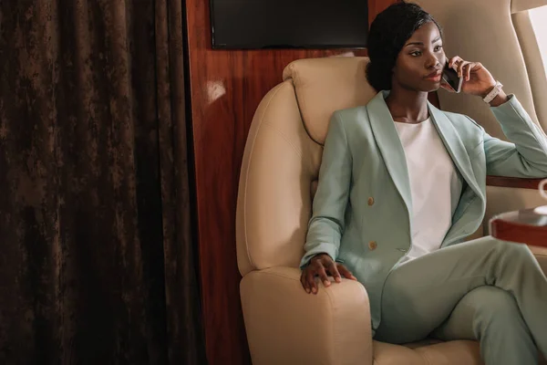 Young, confident african american businesswoman talking on smartphone in private jet — Stock Photo