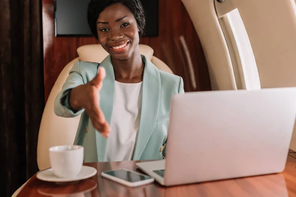 Sonriente mujer de negocios afroamericana mostrando gesto de saludo con la mano extendida - foto de stock