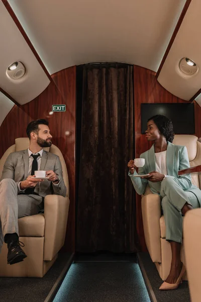 Bel homme d'affaires et séduisante femme d'affaires afro-américaine qui se regarde tout en tenant des tasses de café — Photo de stock