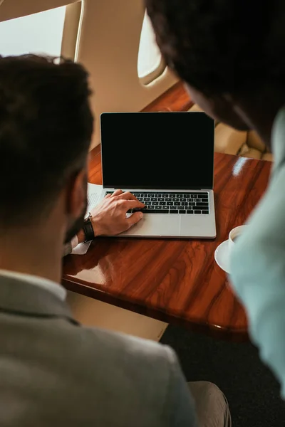 Foco seletivo de empresário e empresária afro-americana olhando para laptop com tela em branco em jato privado — Fotografia de Stock