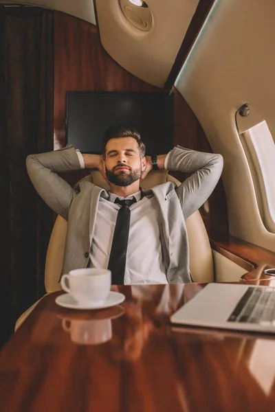 Giovane uomo d'affari a riposo con le mani dietro la testa e gli occhi chiusi in jet privato — Foto stock