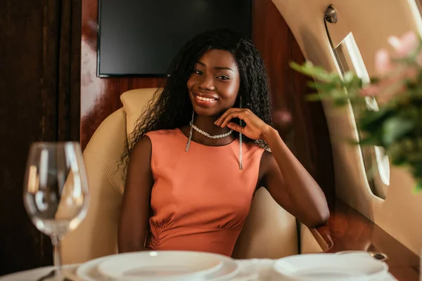 Selective focus of elegant african american woman smiling at camera in private plane — Stock Photo