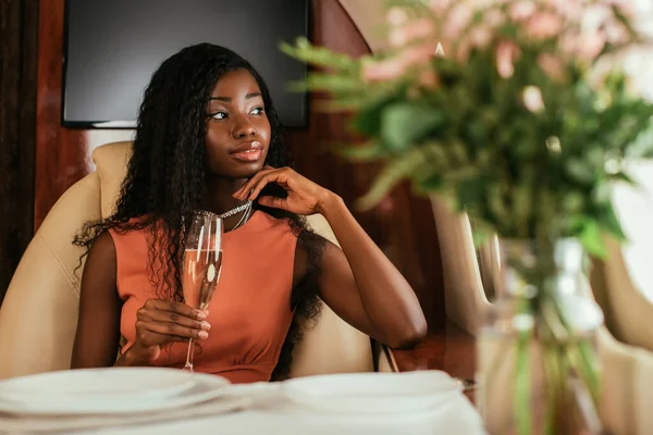 Selective focus of dreamy african american woman holding glass of champagne in private jet — Stock Photo