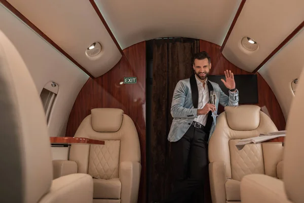 Foyer sélectif de élégant, bel homme agitant la main et tenant une coupe de champagne dans un avion privé — Photo de stock