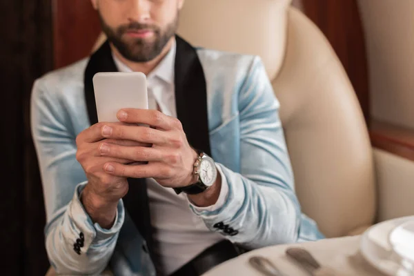 Cropped view of elegant man chatting on smartphone while traveling in private plane — Stock Photo