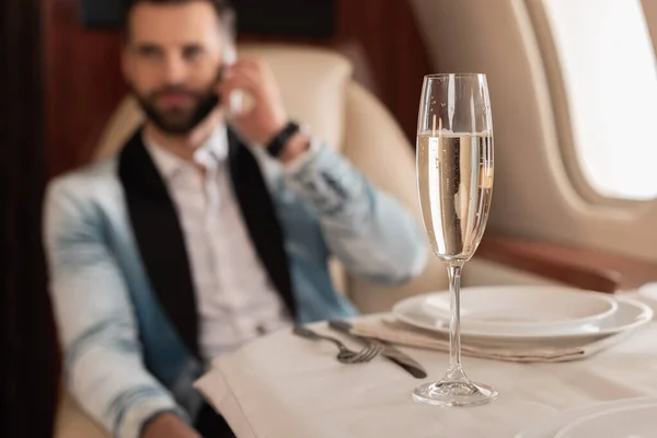 Selective focus of elegant man talking on smartphone near glass of champagne in private jet — Stock Photo