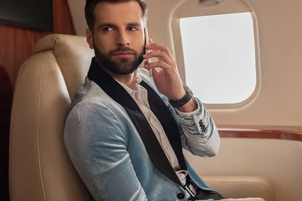 Красивий, впевнений чоловік розмовляє по смартфону під час подорожі в приватному літаку — стокове фото