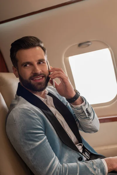 Красивый, элегантный мужчина улыбается, разговаривая по смартфону в частном самолете — стоковое фото