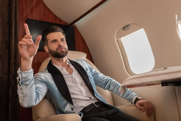 Елегантний, впевнений чоловік показує жест під час виклику повітряного стюардера в приватному реактивному літаку — стокове фото