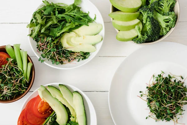 Top view of fresh vegetables and fruits with microgreen in bowls on white wooden surface — Stock Photo