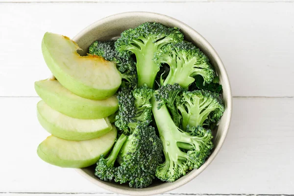 Top view of fresh green apple and broccoli in bowl on white wooden surface — Stock Photo