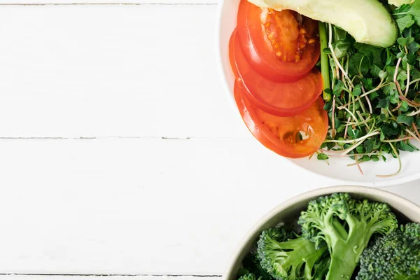 Ansicht von frischem Mikrogrün, Tomaten, Avocado und Brokkoli in Schalen auf weißer Holzoberfläche — Stockfoto