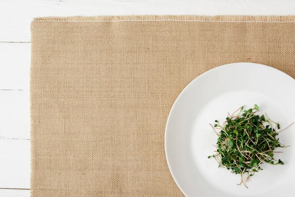 Vue de dessus de microgreen frais sur plaque sur serviette beige sur surface en bois blanc — Photo de stock