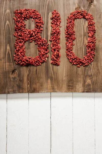 Vista superior de la palabra bio hecha de bayas de goji en la tabla de cortar en la superficie de madera blanca - foto de stock