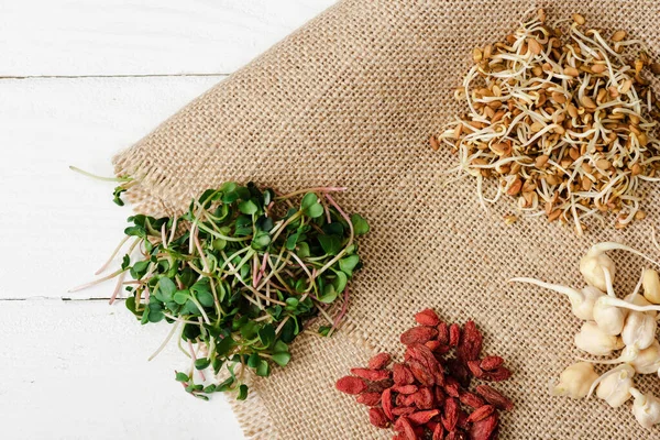 Vista superior de microgreen fresco, brotos e goji bagas em pano de saco na superfície de madeira branca — Fotografia de Stock