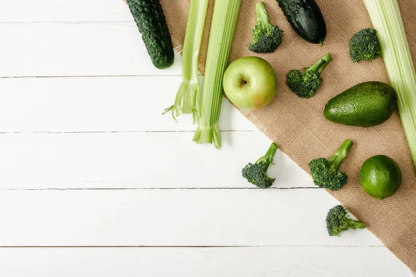 Vista superior de frutas e legumes verdes frescos em pano de saco na superfície de madeira branca — Fotografia de Stock