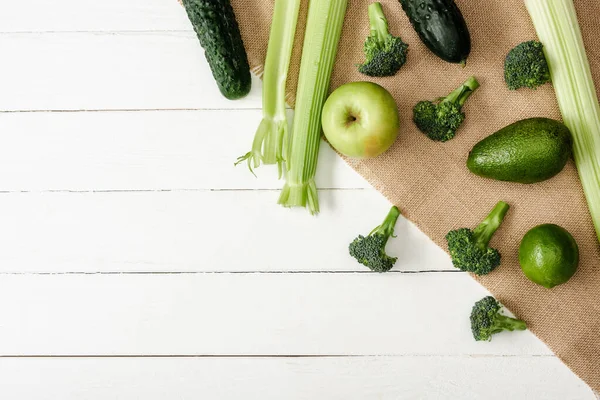 Top view of fresh green fruits and vegetables on sackcloth on white wooden surface — Stock Photo