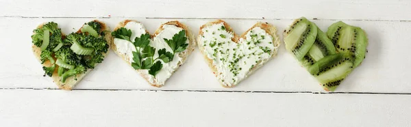 Top view of heart shaped canape with creamy cheese, microgreen, parsley and kiwi on white wooden surface, panoramic crop — Stock Photo
