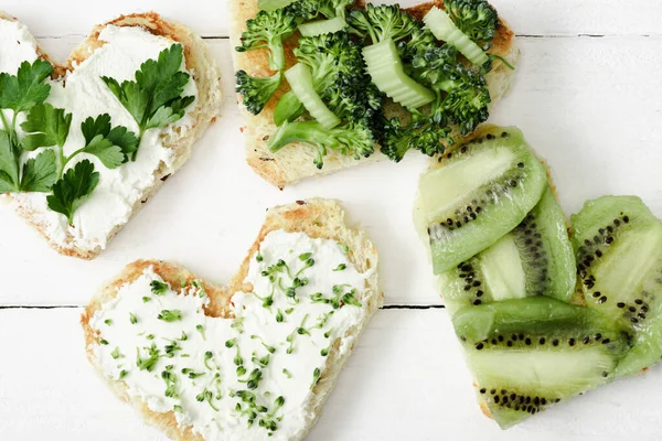 Top view of heart shaped canape with creamy cheese, broccoli, microgreen, parsley and kiwi on white wooden surface — Stock Photo