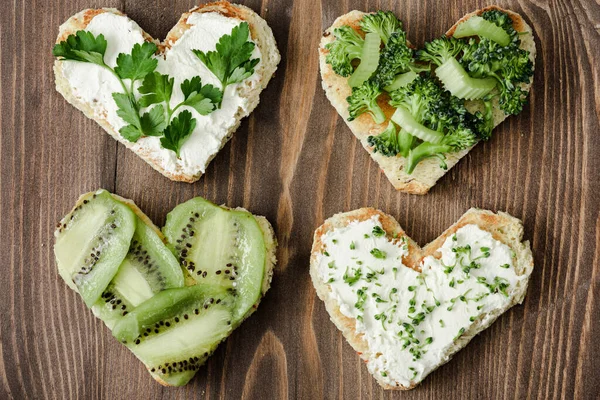 Top view of heart shaped canape with creamy cheese, broccoli, microgreen, parsley and kiwi on wooden surface — Stock Photo