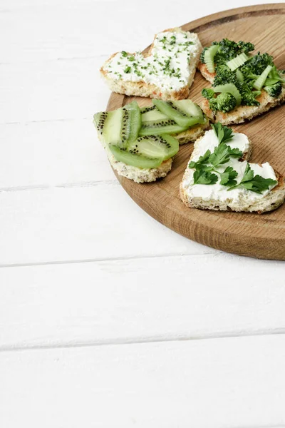 Canape en forme de coeur avec fromage crémeux, brocoli, microvert, persil et kiwi à bord sur une surface en bois blanc — Photo de stock