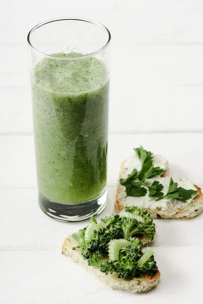 Green smoothie and heart shaped canape with creamy cheese, parsley on white wooden surface — Stock Photo