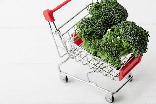 Brócoli verde fresco en el carrito de la compra en la superficie de madera blanca - foto de stock