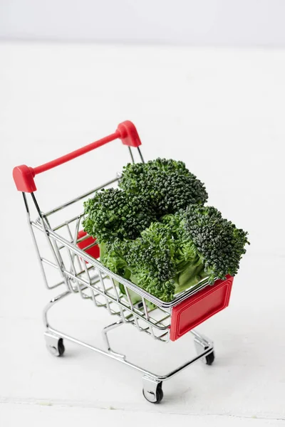 Fresh green broccoli in shopping cart on white wooden surface — Stock Photo