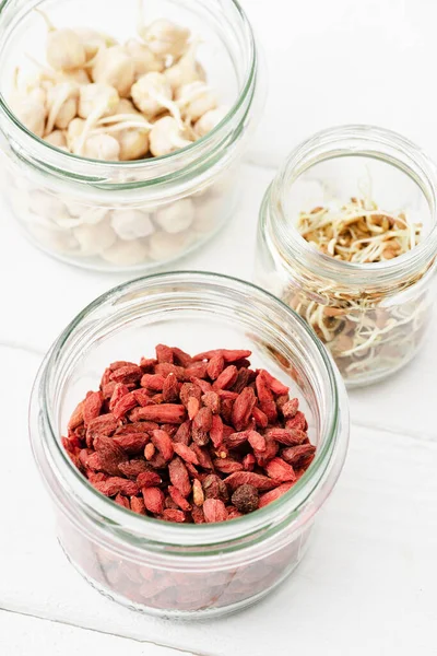 Selective focus of goji berries and sprouts in glass jars on white wooden surface — Stock Photo