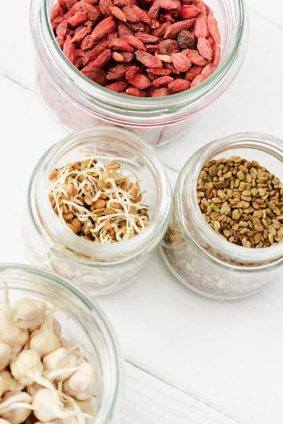 Top view of goji berries and sprouts in glass jars on white wooden surface — Stock Photo