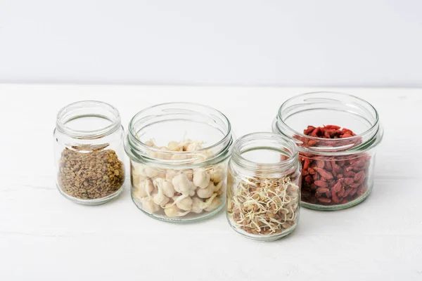 Goji berries and sprouts in glass jars on white wooden surface — Stock Photo