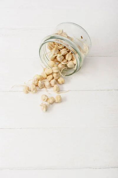 Sprouts scattered from glass jar on white wooden surface — Stock Photo