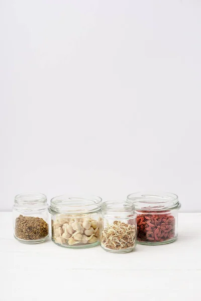 Goji berries and sprouts in glass jars on white wooden surface — Stock Photo