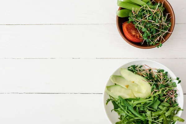 Draufsicht auf frisches Gemüse mit Avocado und Microgreen in Schalen auf weißer Holzoberfläche — Stockfoto