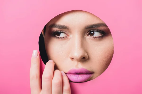 Mujer con ojos humeantes y labios rosados mirando hacia otro lado del agujero y tocando papel - foto de stock