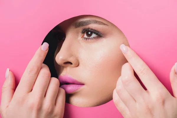 Woman with pink lips looking across hole and touching colorful paper with hands — Stock Photo