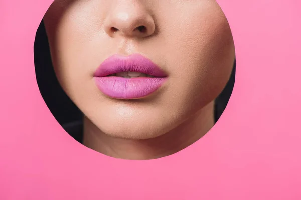 Vista recortada de cara femenina con labios rosados en agujero redondo en papel - foto de stock