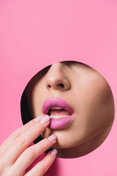 Cropped view of woman touching pink lips across hole in paper — Stock Photo