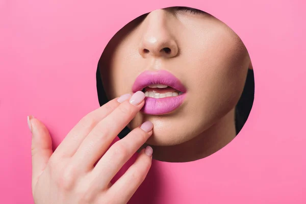 Vista recortada de la mujer tocando los labios rosados a través del agujero en papel colorido - foto de stock