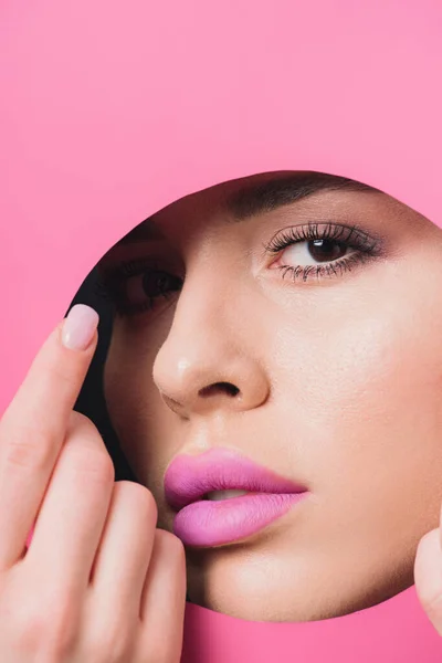 Mulher com lábios cor-de-rosa olhando para a câmera através do buraco redondo e tocando papel colorido com a mão — Fotografia de Stock