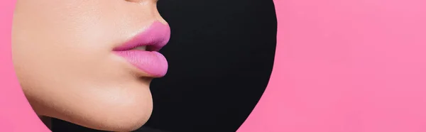 Cropped view of female face with pink lips in round hole in paper on black background, panoramic shot — Stock Photo