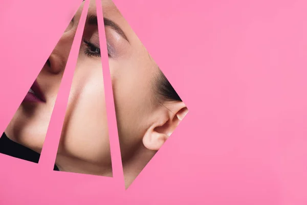 Female face across triangular holes in pink paper — Stock Photo
