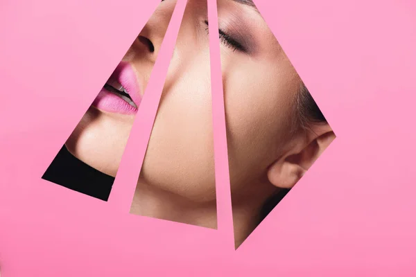 Female face with pink lips and closed eyes across triangular holes in paper on black — Stock Photo