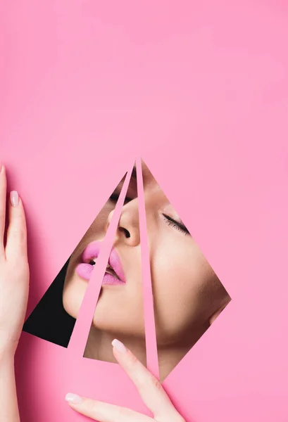 Woman with pink lips and closed eyes across triangular holes touching paper on black — Stock Photo