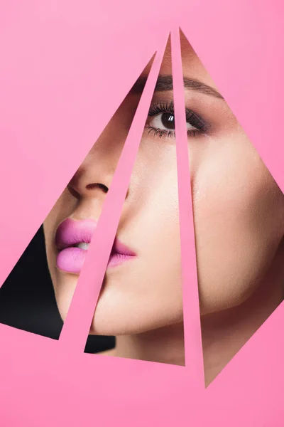 Mädchen mit rauchigen Augen und rosa Lippen blickt über dreieckige Löcher in Papier auf schwarz — Stockfoto