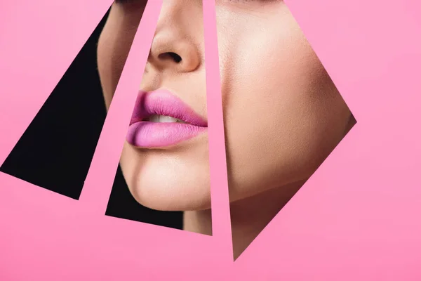 Cropped view of female face with pink lips across triangular holes in paper on black background — Stock Photo