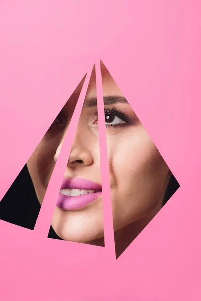 Женщина с дымчатыми глазами и розовыми губами, улыбающаяся через треугольные отверстия в бумаге на черном фоне — стоковое фото