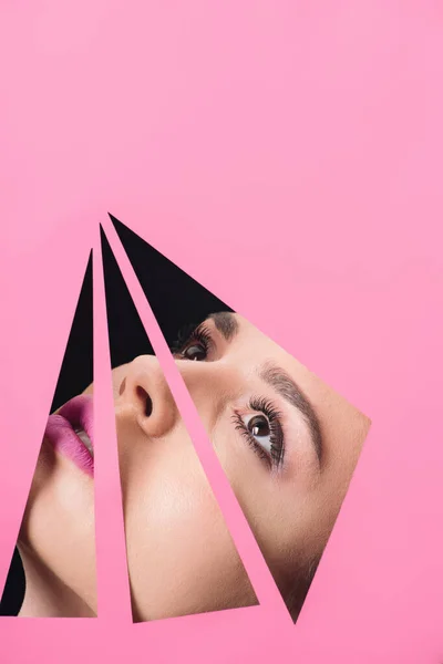 Female face with makeup across holes in pink paper on black background — Stock Photo